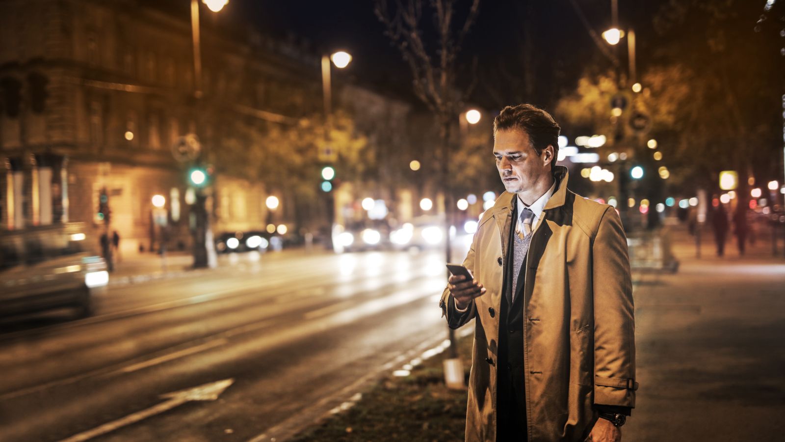 A professional checking his phone on a city street at night, representing an insurance lead that arrives after business hours